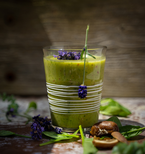 KI generiert: Ein grüner Smoothie im Glas, dekoriert mit Lavendel, Spinatblättern und Kastanien daneben.