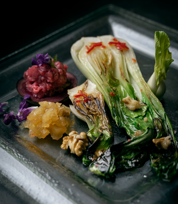 KI generiert: Gegrilltes Pak Choi mit Nüssen, Ananasstücken, rotem Tatar und essbaren Blüten auf Glasplatte.