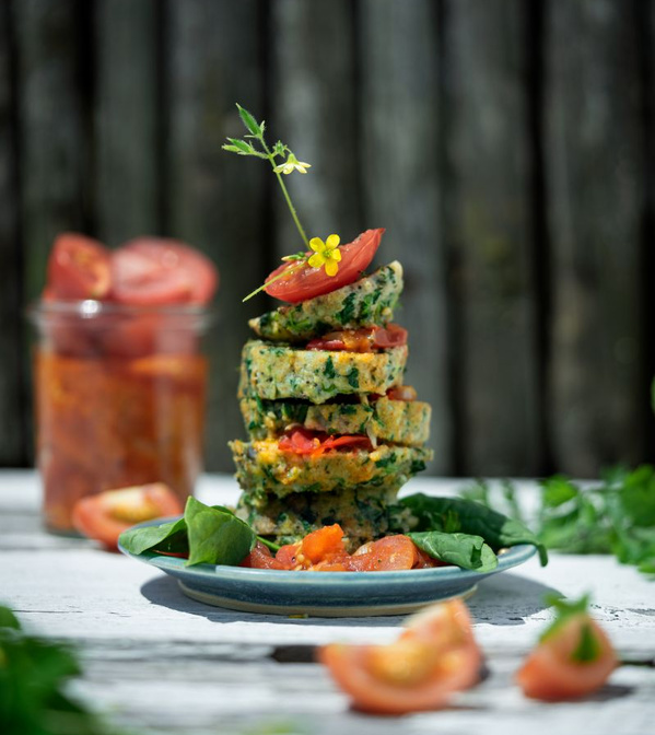 KI generiert: Ein Stapel vegetarischer Puffer mit Tomaten und Kräutern auf einem Teller, im Freien angerichtet.