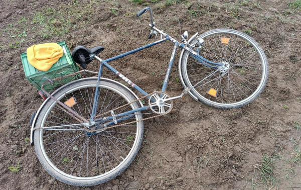 KI generiert: Ein altes Fahrrad mit Kiste und gelbem Tuch liegt im braunen Schlamm.