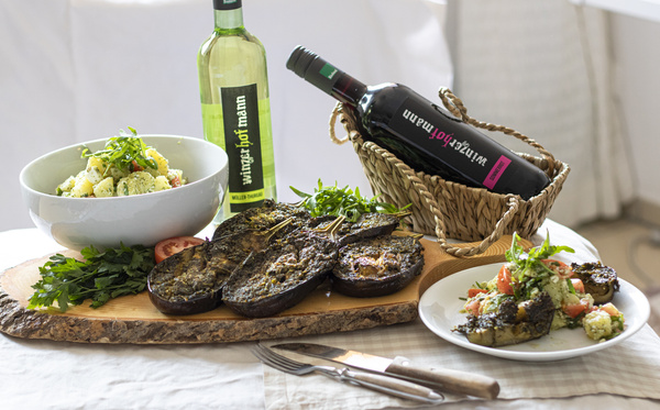 KI generiert: Gerichte aus Auberginen mit Salat und Weinflaschen auf einem Tisch. Text: "wintgerhof mann".